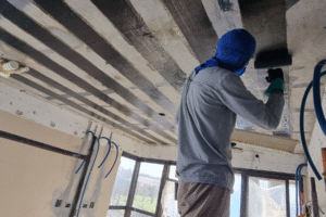 Operário aplicando manta de fibra de carbono com rolo para reforço estrutural em laje de concreto.