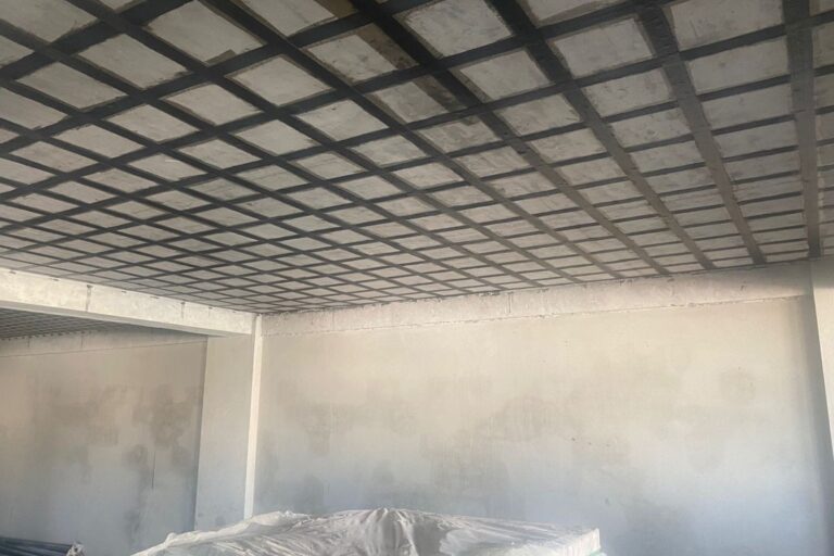 Aplicação de laminados de fibra de carbono (CFRP) para reforço estrutural de vigas e lajes de concreto armado em edificação em construção.